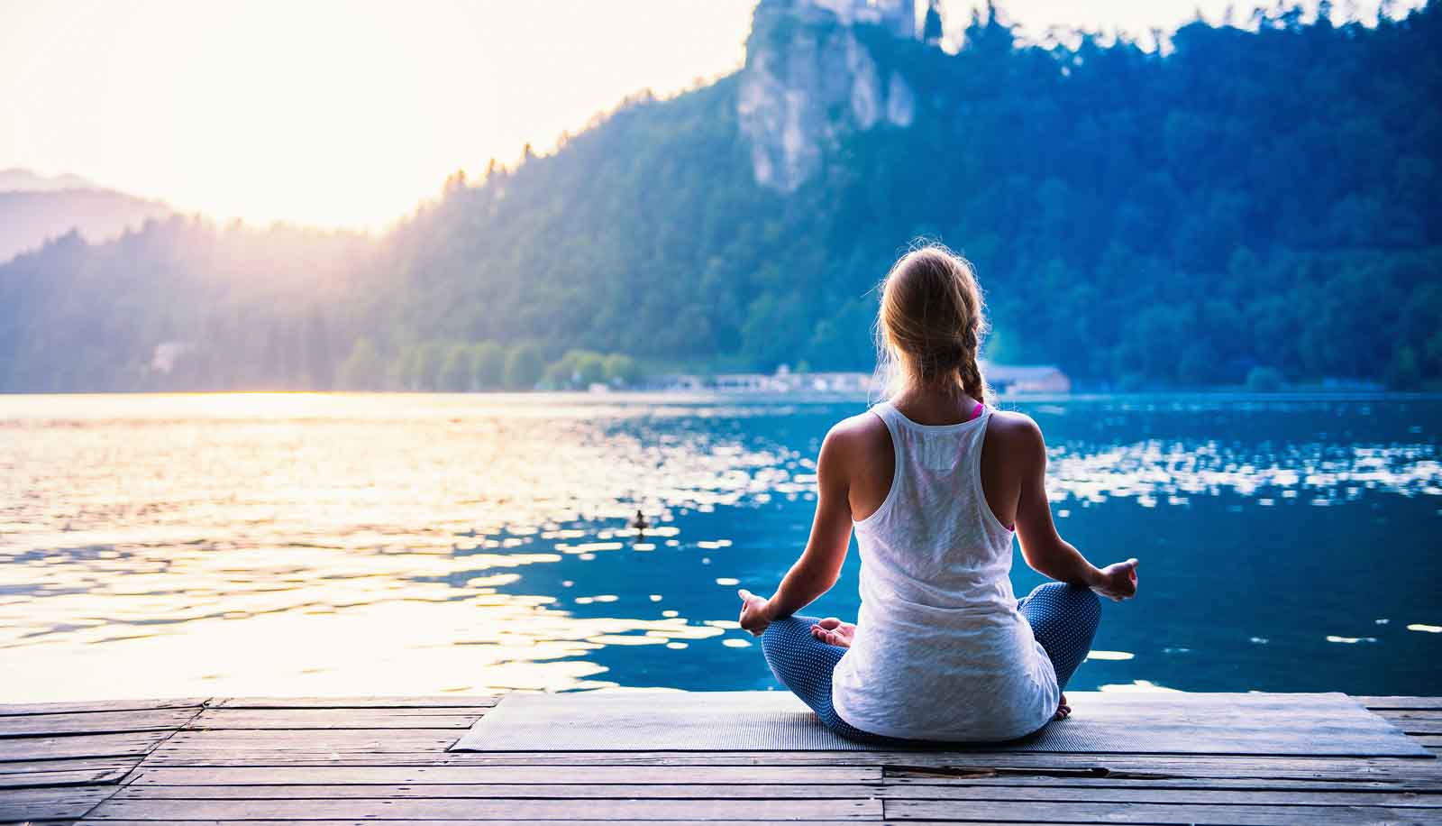 woman meditating on dock next to lake